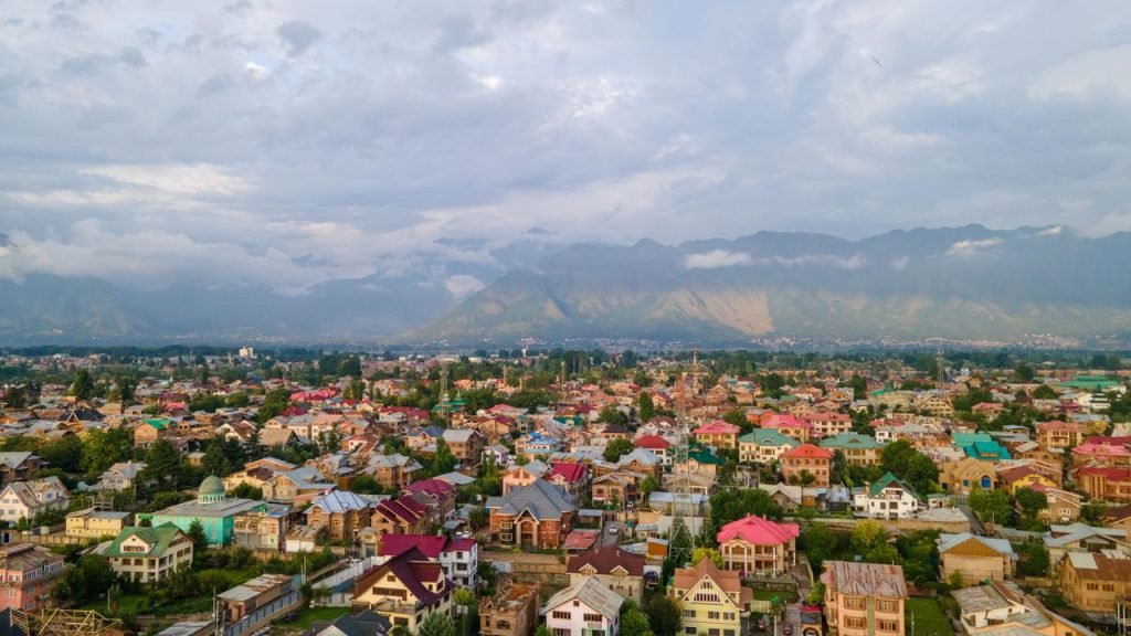 Stunning aerial view of colorful Srinagar city with Himalayan backdrop under cloudy skies.