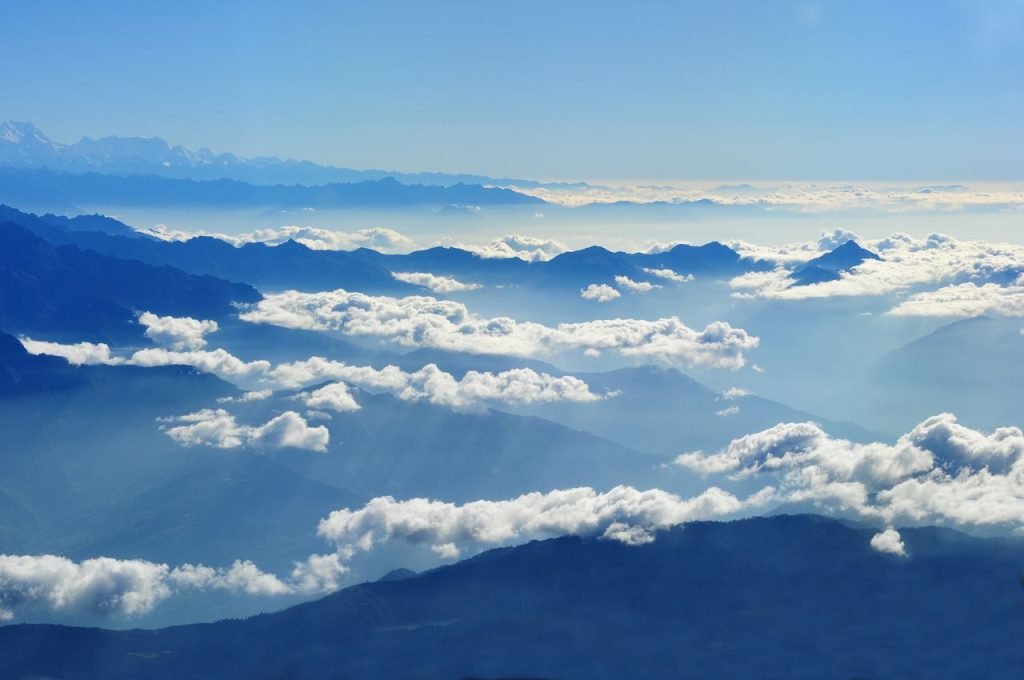 Stunning aerial view of mountains and clouds under a bright blue sky.